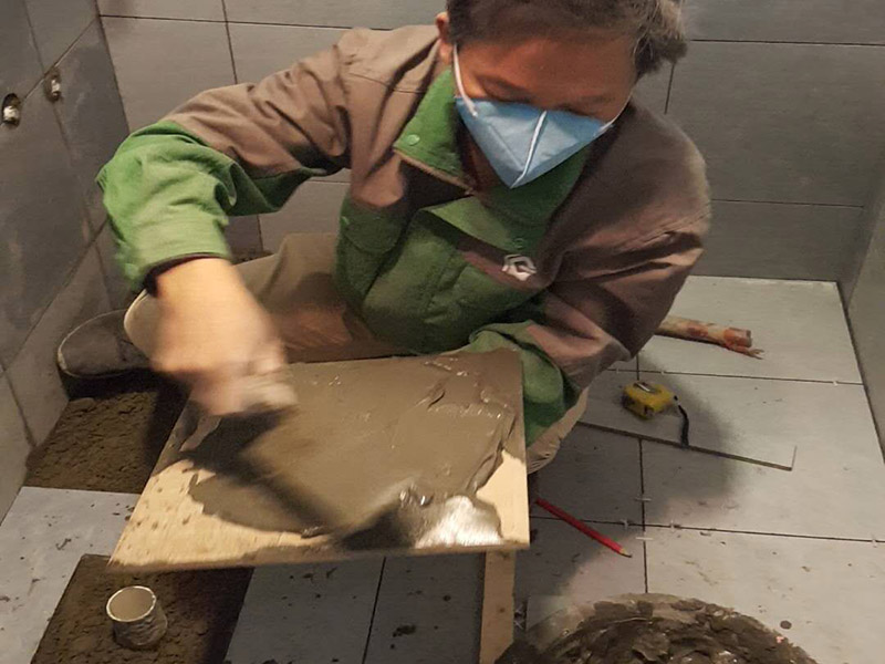 廁所貼地磚：
1、基層處理：把沾在基層上的浮漿、落地灰等用暫子或鋼絲刷清理掉，再用掃帚將浮土清掃干凈。
2、找標高：根據(jù)水平標準線和設(shè)計厚度，在四周墻、柱上彈出面層的上平標高控制線。
3、排磚：將房間依照磚的尺寸留縫大小，排出磚的放置位置，并在基層地面彈出十字控制線和分格線。
4、鋪設(shè)結(jié)合層砂漿：鋪設(shè)前應(yīng)將基底濕潤，并在基底上刷一道素水泥漿或界面結(jié)合劑，隨刷隨鋪設(shè)攪拌均勻的干硬性水泥砂漿。
5、鋪磚：將磚放置在于拌料上，用橡皮錘找平，之后將磚拿起，在干拌料上澆適量素水泥漿，同時在磚背面涂厚度約lnm的素水泥膏，再將磚放置在找過平的干拌料上，用橡皮錘按標高控制線和方正控制線坐平坐正。
6、鋪磚時應(yīng)先在房間中間按照十字線鋪設(shè)十字控制磚，之后按照十字控制磚向四周鋪設(shè)，并隨時用2m靠尺和水平尺檢查平整度。大面積鋪貼時應(yīng)分段、分部位鋪貼。
7、養(yǎng)護：當磚面層鋪貼完24h內(nèi)應(yīng)開始澆水養(yǎng)護，養(yǎng)護時間不得小于7d。